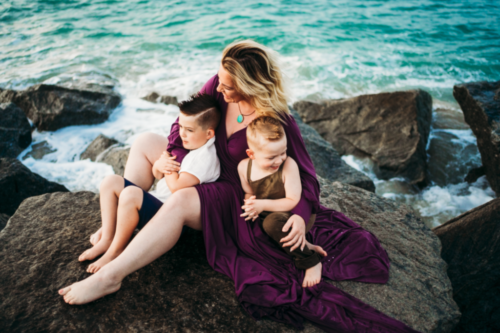 Image of mother and two sons sitting on a rock near the ocean